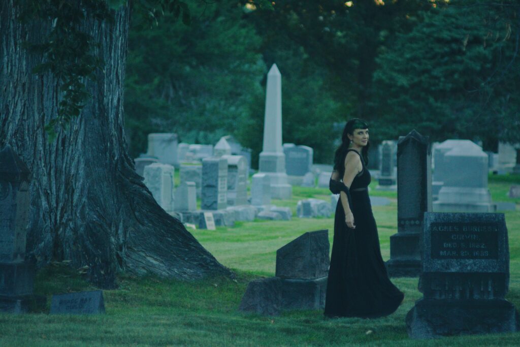 Rene wanders through the tombstones at a distance, looking over her shoulder to smile at the camera.