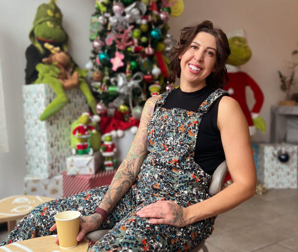 Sitting in front of the very Grinchy Christmas tree at Ti Cafe, Hallie smiles with her coffee in hand.