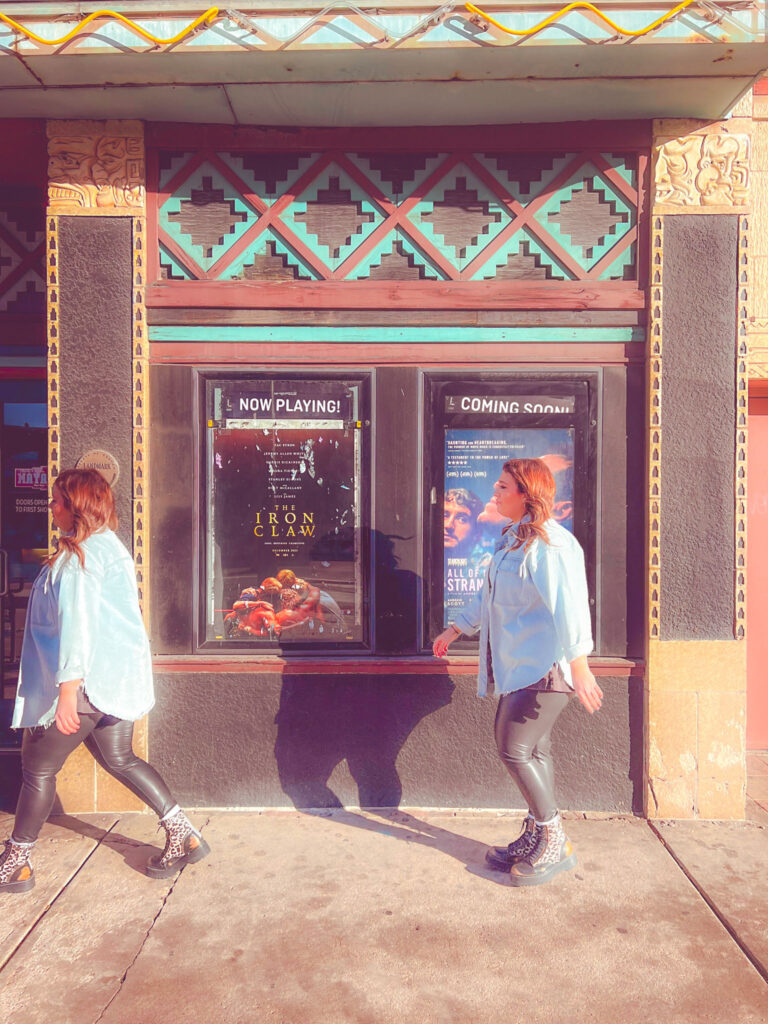 Two different poses of Megan walk past the theater's movie posters outside.